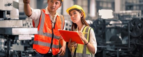 Engineer wearing safety vest controlling machine working talking with assistant engineer worker checking safety first for labour workers. Safety officer check machine in factory.